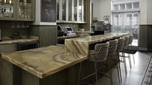 Uma área de bar com bancada de mármore, banquetas e um armário para bebidas.