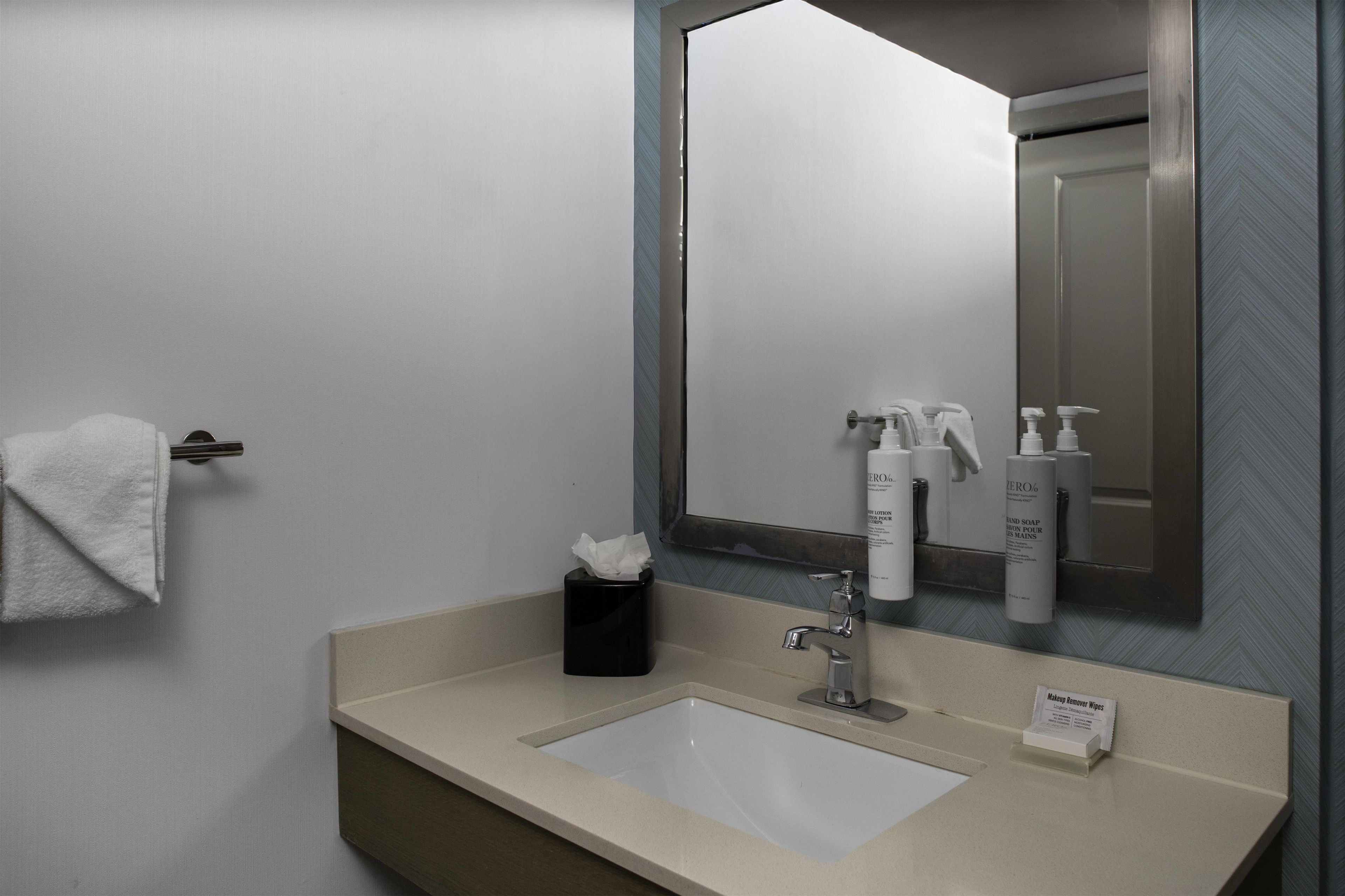 Une salle de bain équipée d’un lavabo, d’un miroir, d’une serviette et d’articles de toilette.