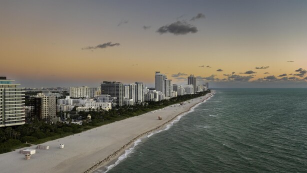 Paisagem costeira com edifícios altos, uma praia de areia e o oceano.