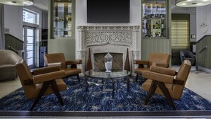Um hall com lareira, poltronas de couro, mesa de centro de vidro e tapete estampado.