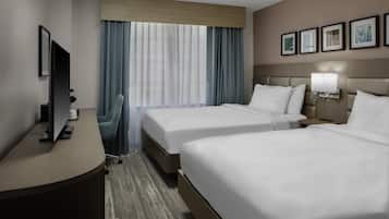 A hotel room with two beds, a desk, a chair, a TV, and a window with curtains.