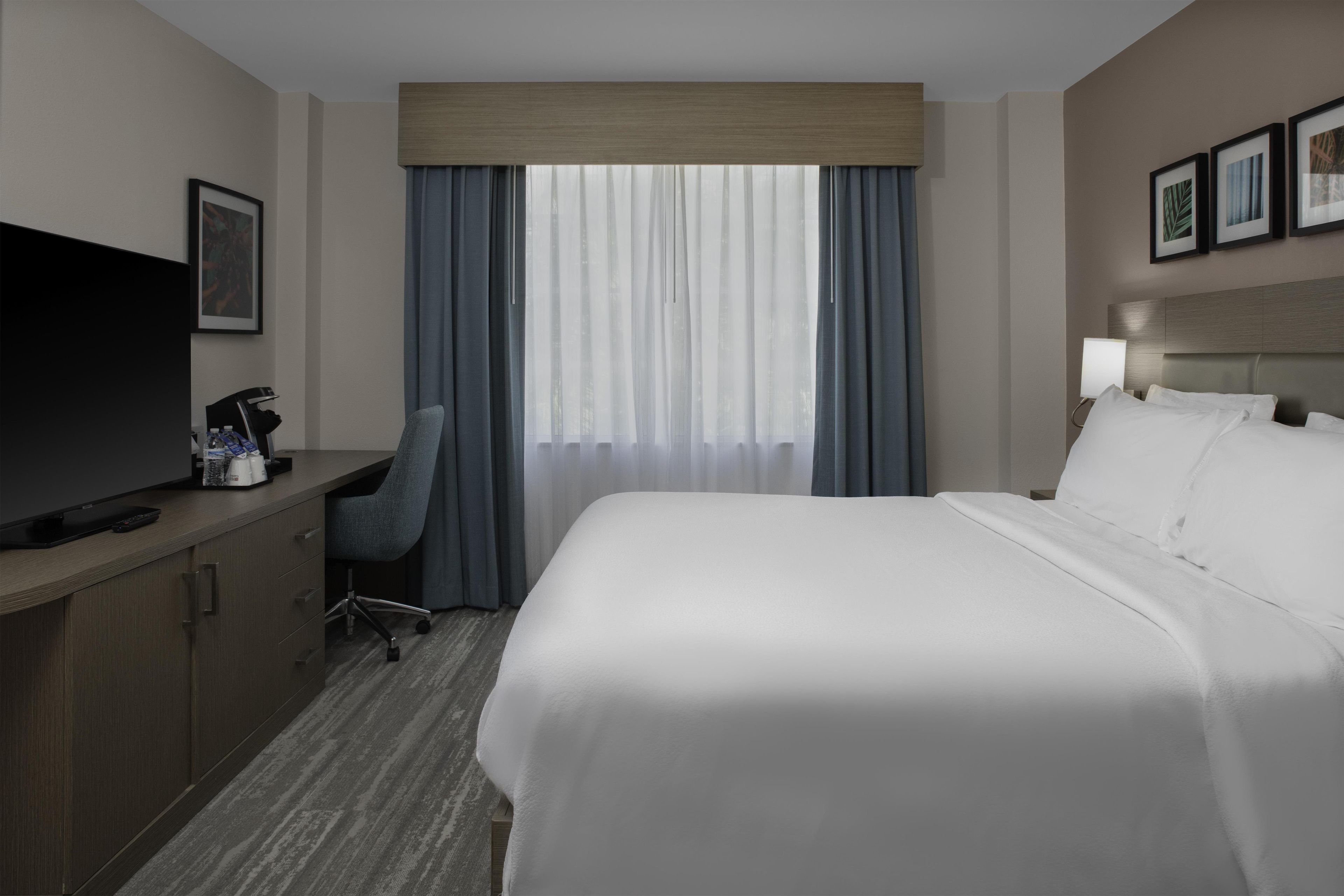 A hotel room with a bed, a desk with a television, a chair, and a window with curtains.