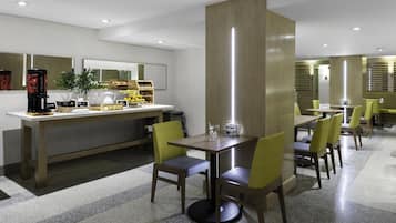 A modern hotel dining area with a coffee station, seating arrangements, and a large mirror.