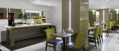 A modern hotel dining area with a coffee station, seating arrangements, and a large mirror.