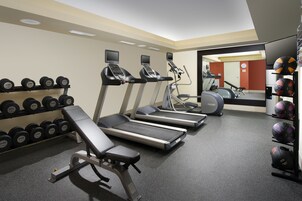 Un gimnasio con cintas de correr, una banca y un estante con mancuernas.