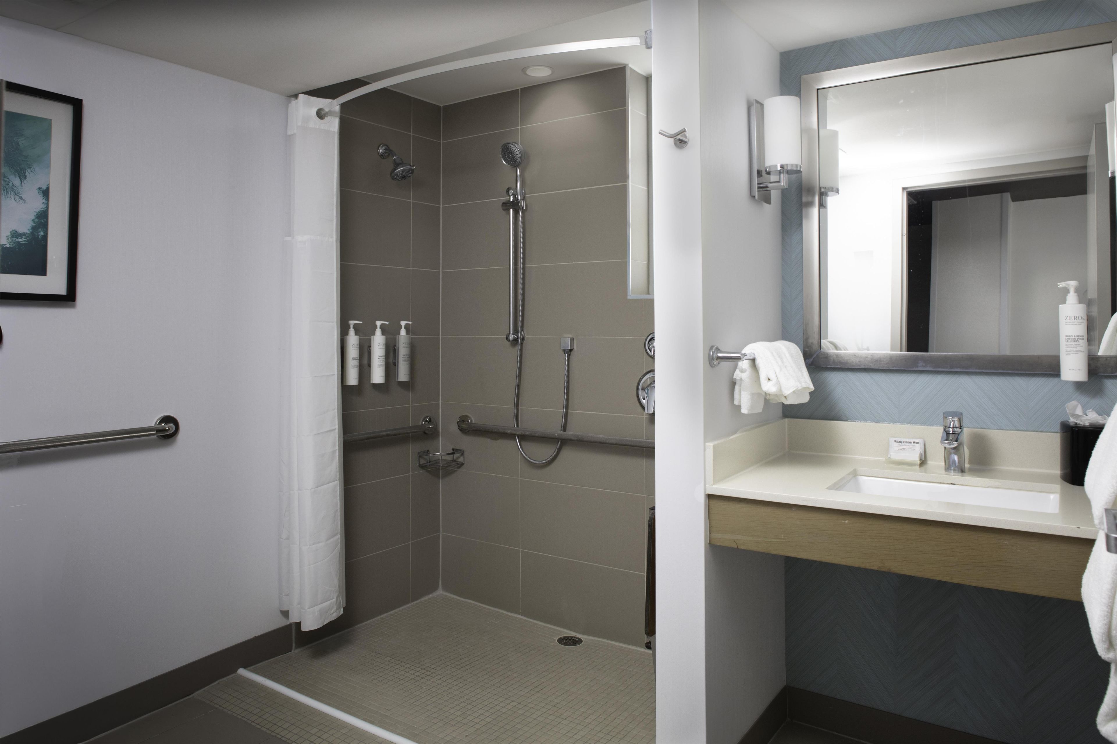 A hotel bathroom with a shower, a sink, and a mirror.