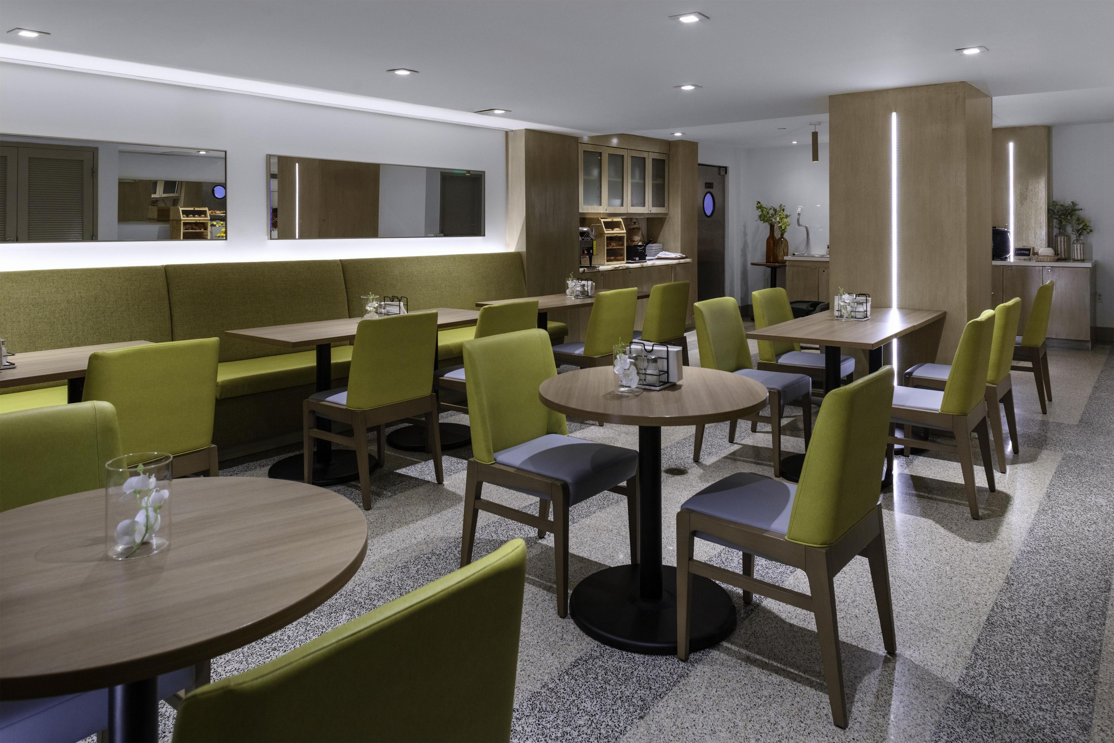 Un espace repas moderne avec des banquettes et des tables, un bar et une cuisine visible au fond.