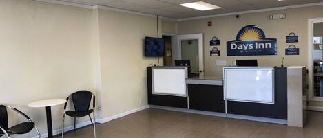Un área de recepción con mostrador, un televisor montado en la pared y un cartel de Days Inn by Wyndham.