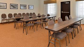 A conference room with multiple tables and chairs, framed pictures on the wall, and a door with an exit sign.