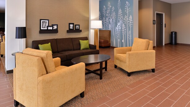 Un hall con un sofá marrón, dos sillones, una mesa de centro y una pared decorada con un mural floral.