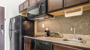 Una cocina moderna con alacenas de madera oscura, un refrigerador negro, un microondas, un lavavajillas, un protector contra salpicaduras de azulejos y un lavamanos de acero inoxidable.