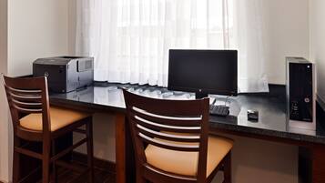 Un espacio de trabajo con dos sillas de madera, una computadora de escritorio, un monitor e impresora.