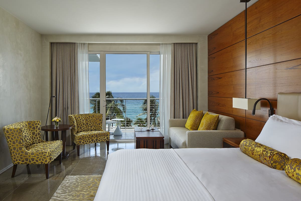 A hotel room with a large bed, two armchairs, a sofa, a small table, and a view of the ocean.