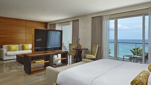 Quarto de hotel com cama grande, televisão, sofá, mesinha e varanda com vista para o mar.