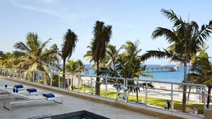 Área da piscina com espreguiçadeiras, posto de salva-vidas e vista para a praia e o oceano.
