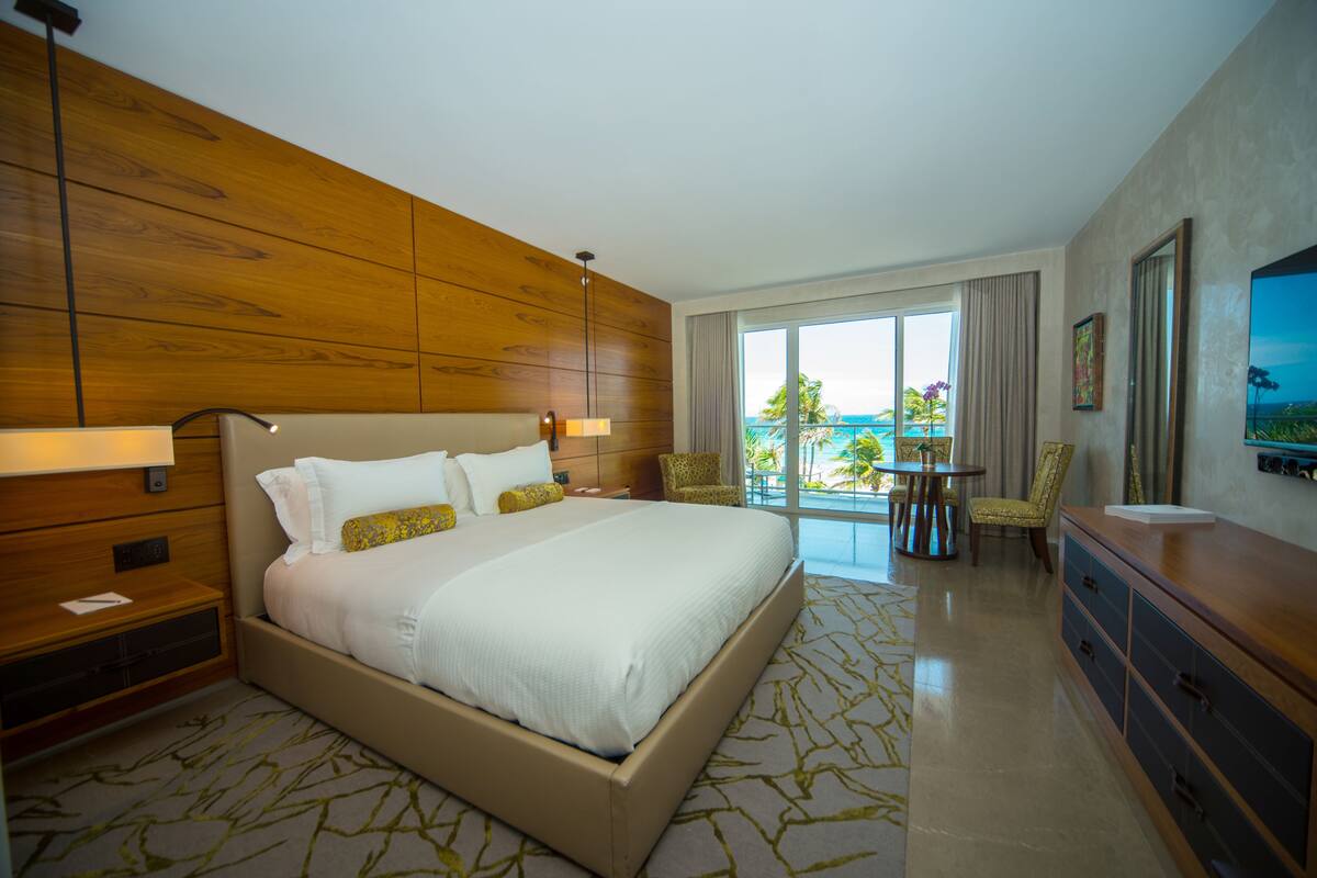 A hotel room with a large bed, wooden paneling, a balcony with a view, and a television.