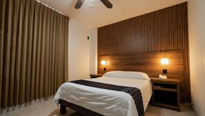 A neatly arranged bedroom with a large bed, wooden headboard, two bedside tables with lamps, and a curtain on the window.
