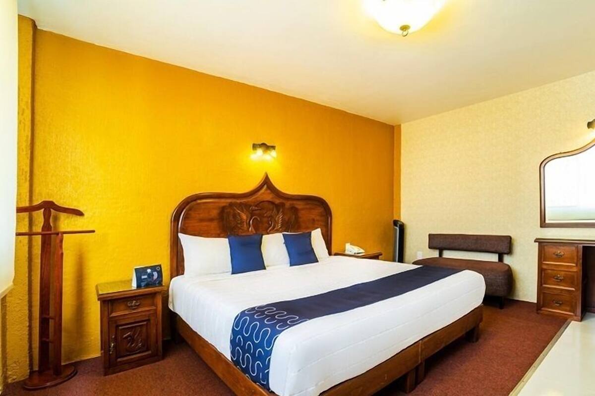 A hotel room with a wooden bed, a nightstand, a dresser, and a mirror.