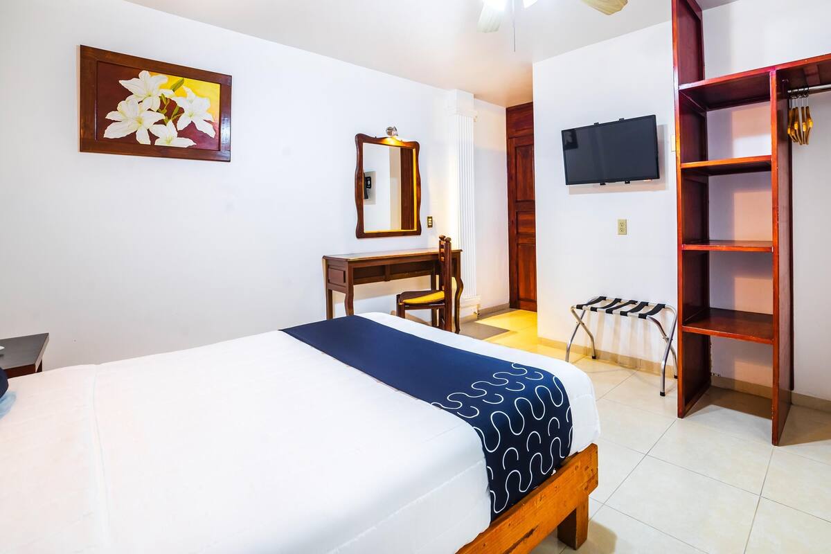 A hotel room with a bed, a desk, a chair, a wardrobe, a television, and a ceiling fan.