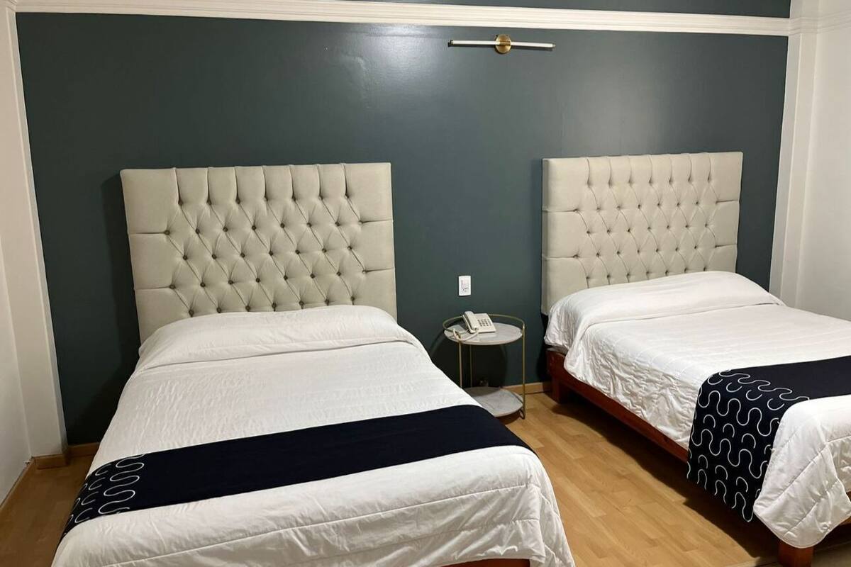 A hotel room with two beds, each with a tufted headboard, white bedding, and a dark blue accent.