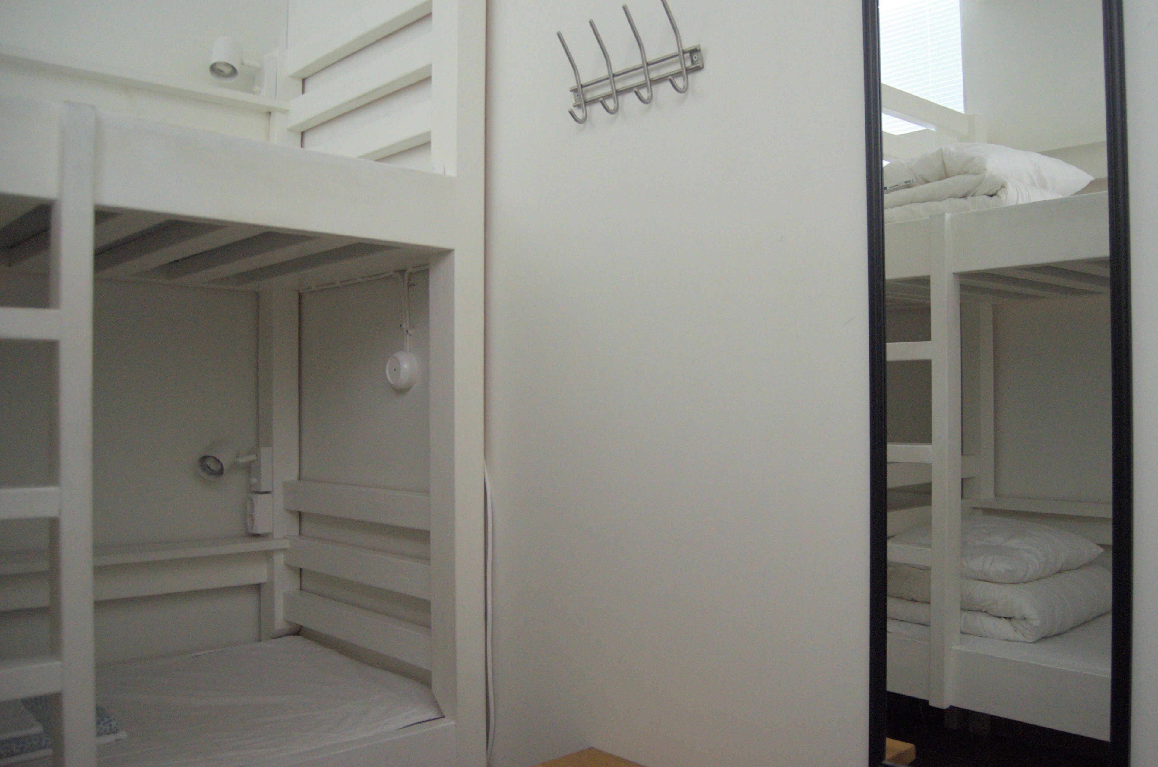 A bunk bed room with a white color scheme, a hook for hanging items, and a small shelf.