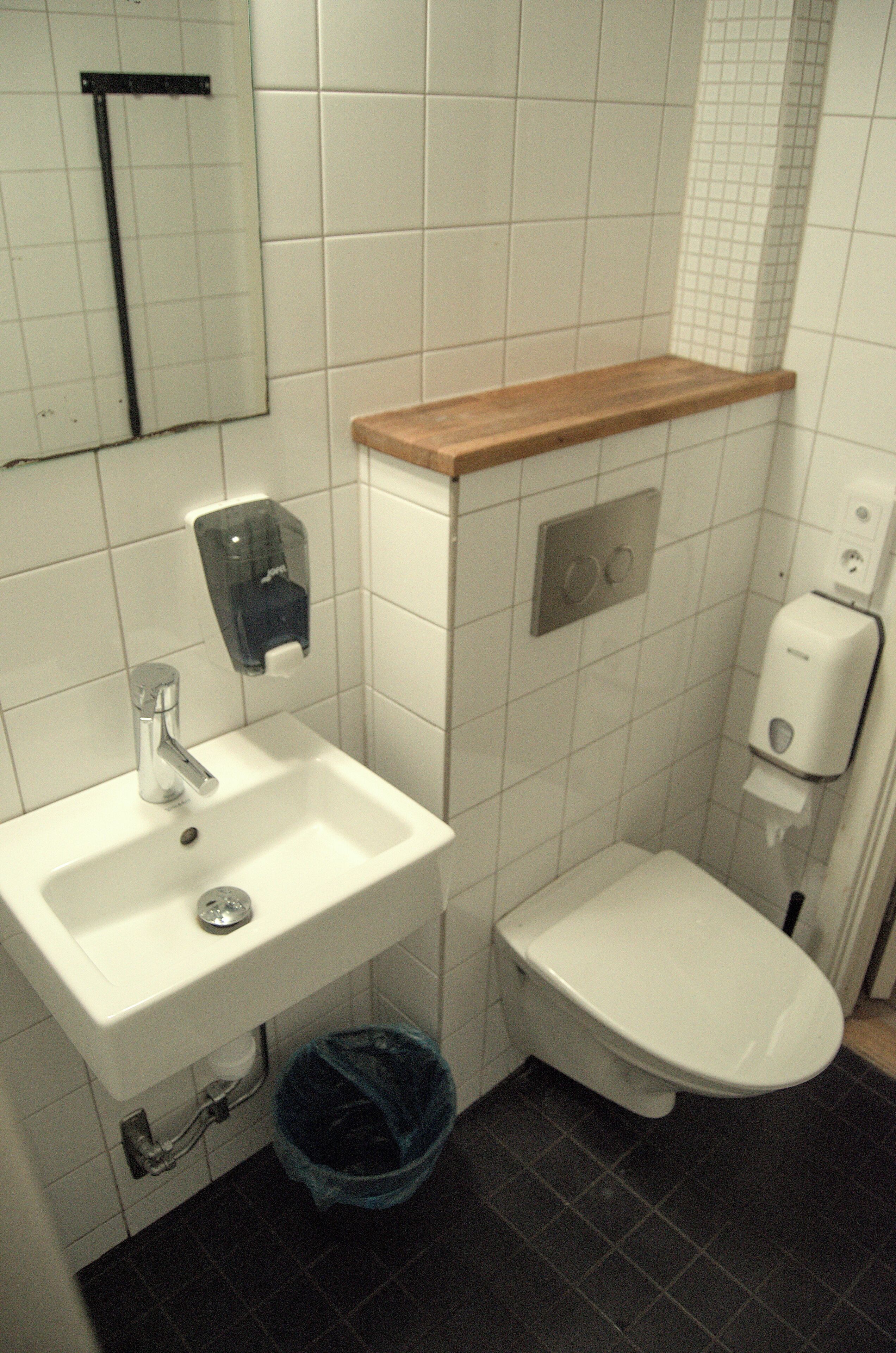 A bathroom with a white sink, a toilet, and a soap dispenser.
