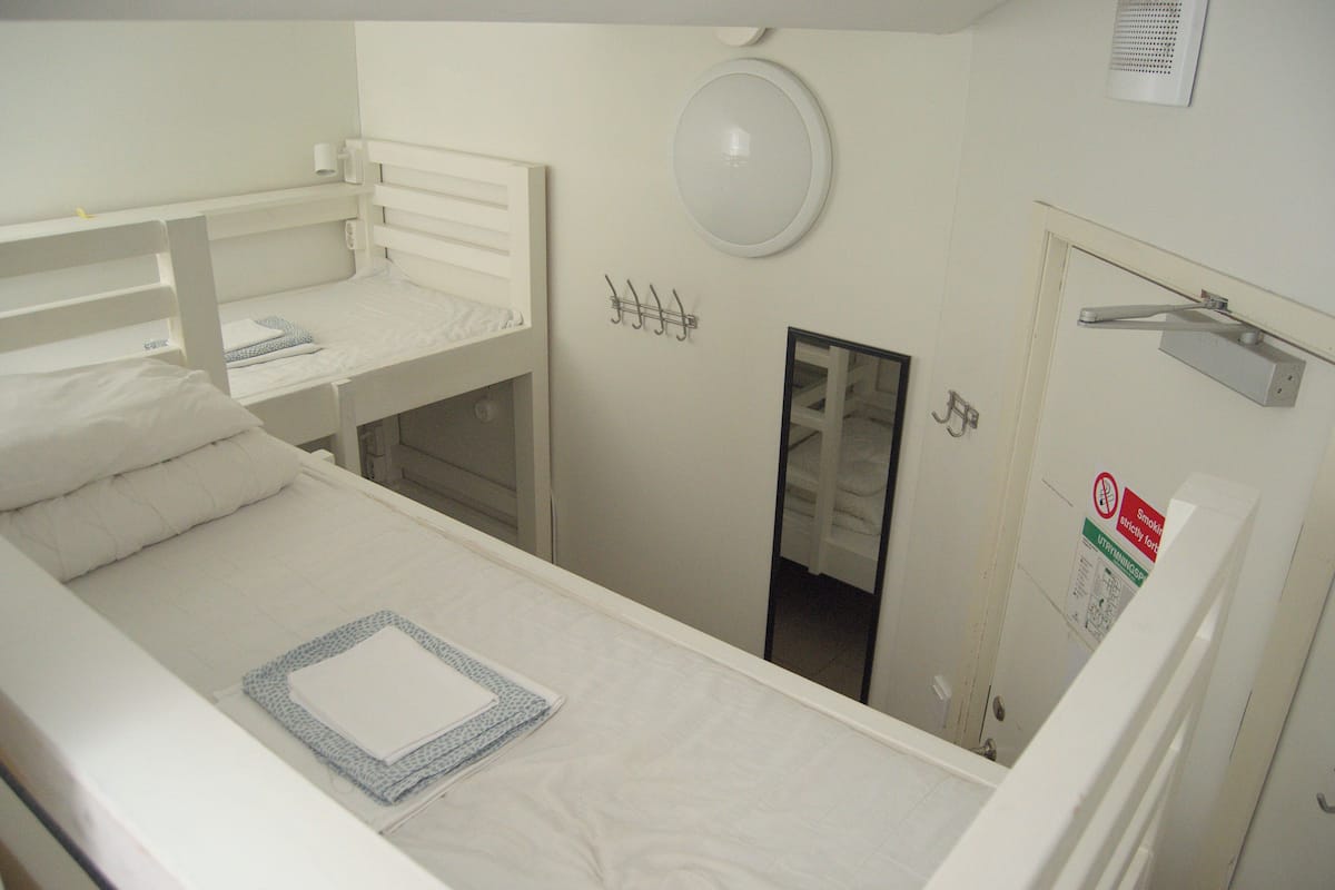 Asuntolatyylinen huone, jossa on kerrossängyt, peili, naulakko ja kyltillä varustettu ovi.
