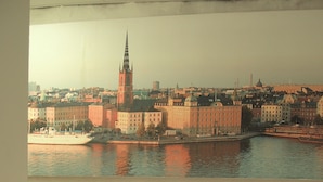 A bed with a folded towel, a view of a cityscape with a prominent tower across a river. - Hostel Dalagatan (Stockholm)