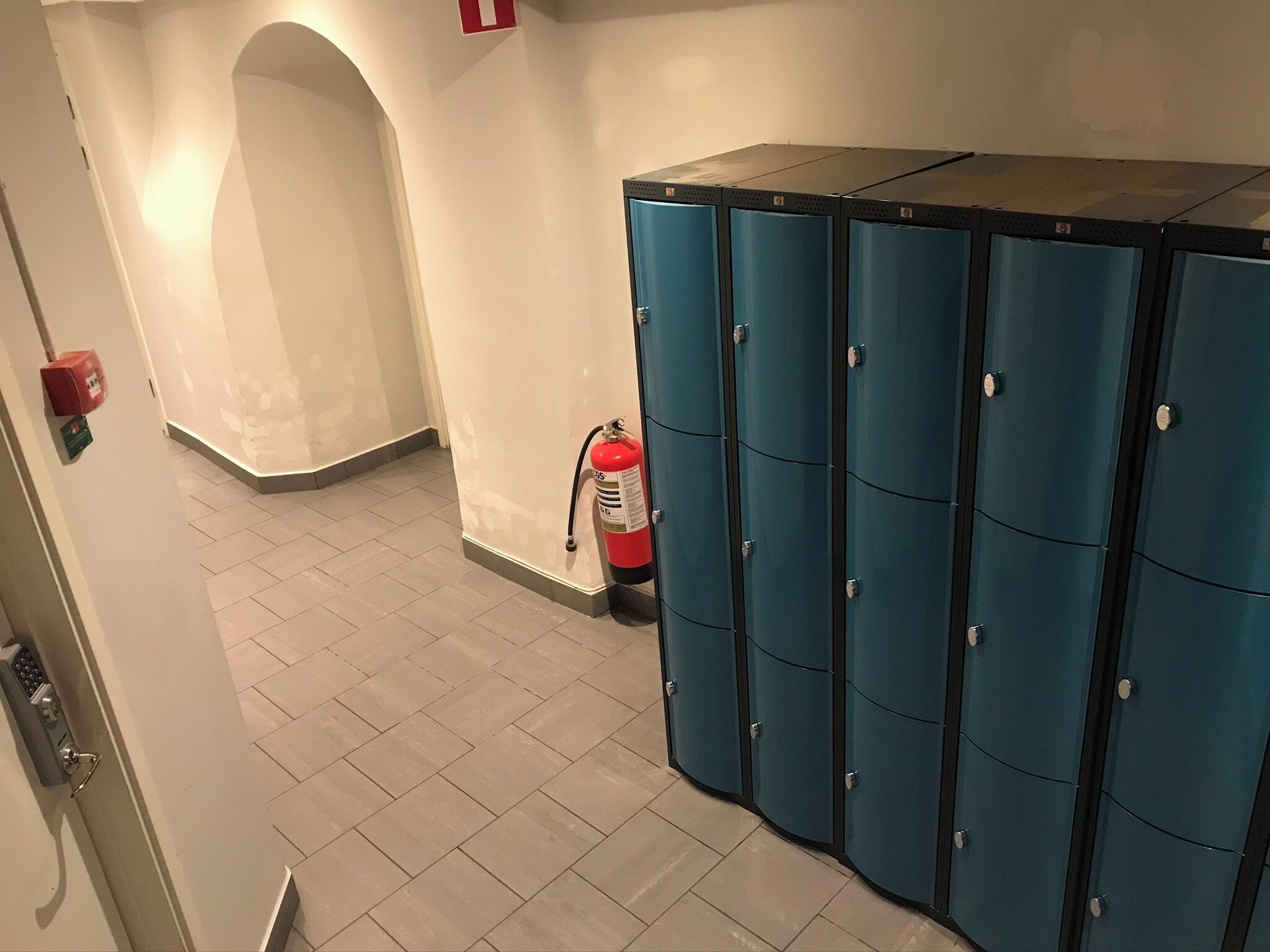 Ein Flur mit blauen Schließfächern, einem Feuerlöscher und einer Tür mit Schlüsselkartenleser.