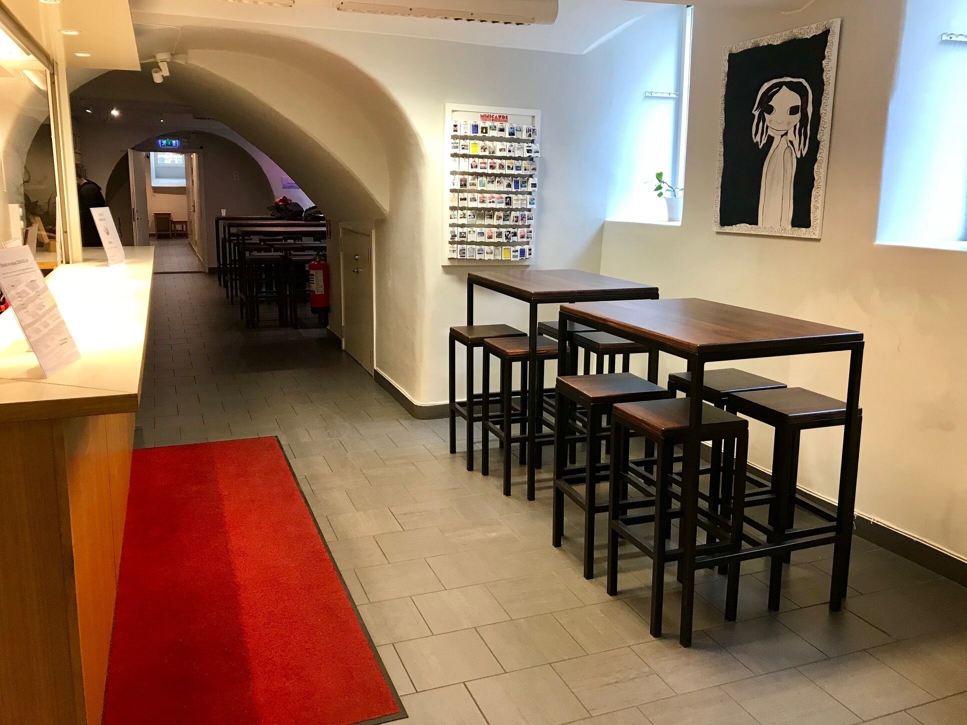A modern interior with a reception desk, a red carpet, and a wall with postcards.