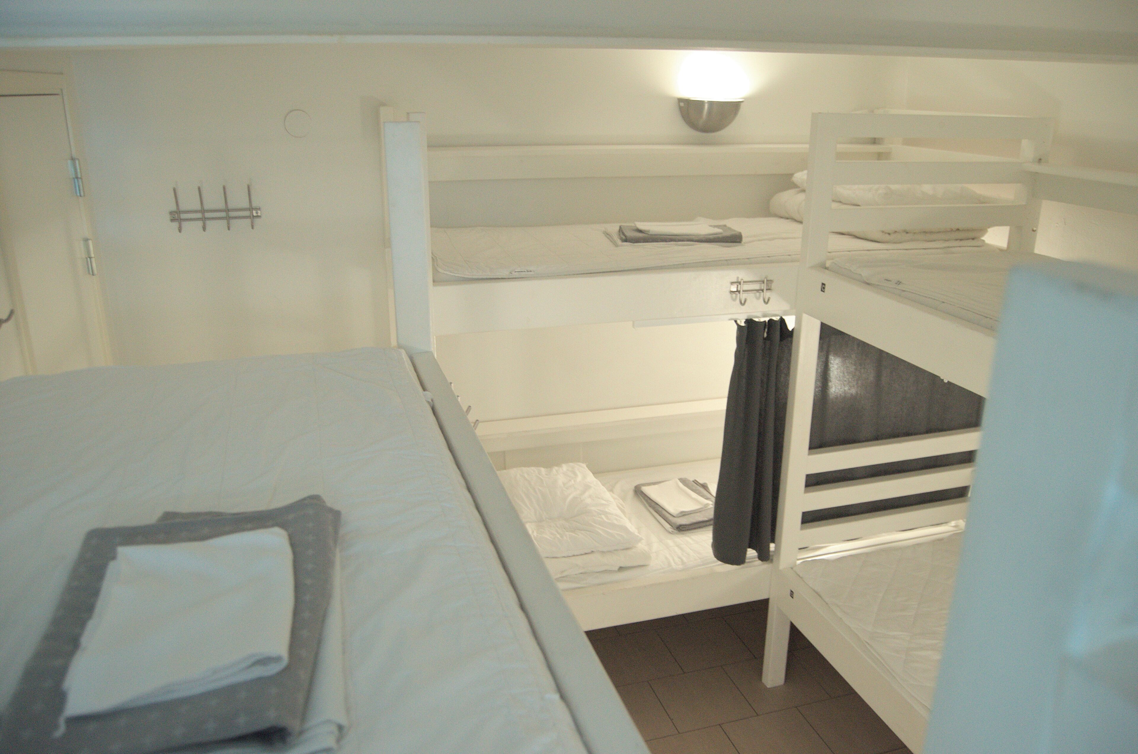 A bunk bed room with a single bed on the left and a bunk bed on the right. There is a wall-mounted light above the bunk bed and a towel rack on the wall.