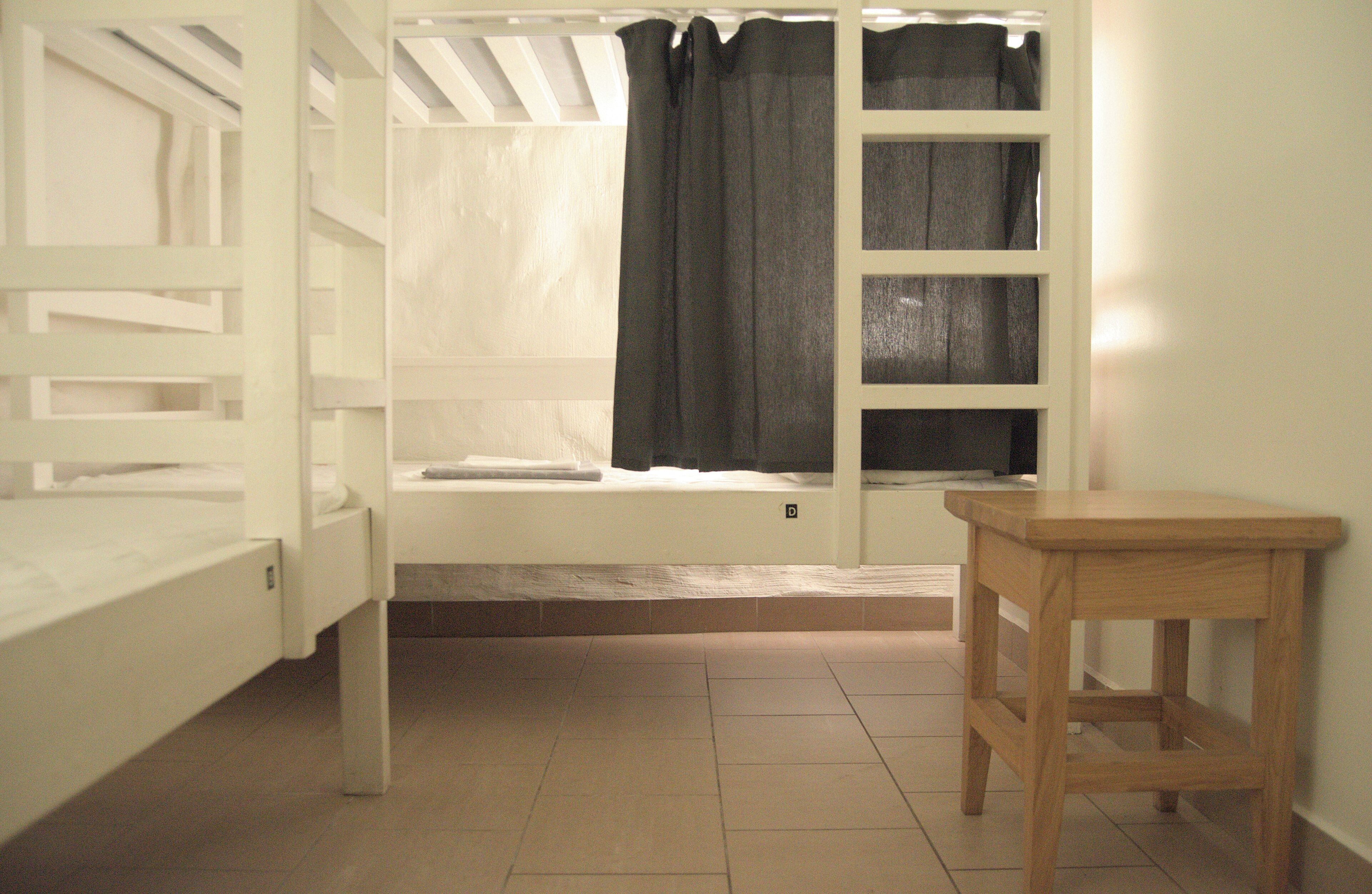A room with a bunk bed, a window with curtains, a wooden table, and a tiled floor.