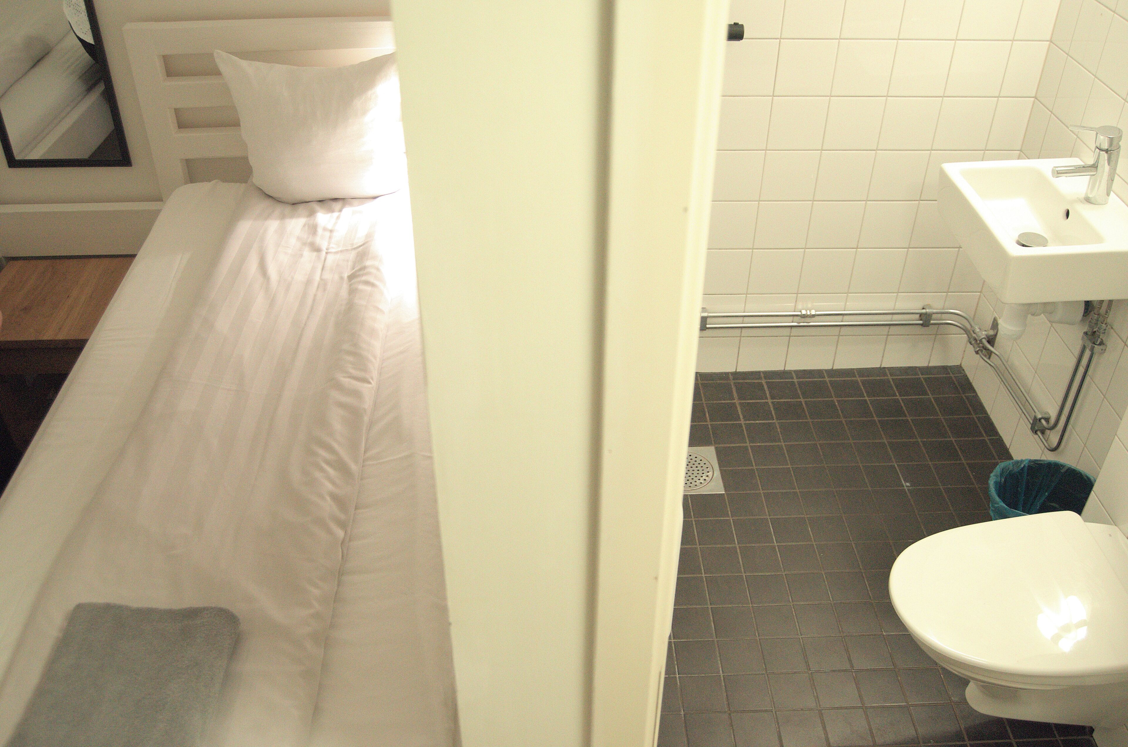 Una habitación de hotel con una cama, un lavamanos blanco y un inodoro.