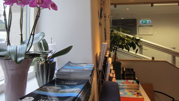 A reception area with a potted orchid, a stack of magazines, and a staircase leading to an upper floor. - Hostel Dalagatan (Stockholm)
