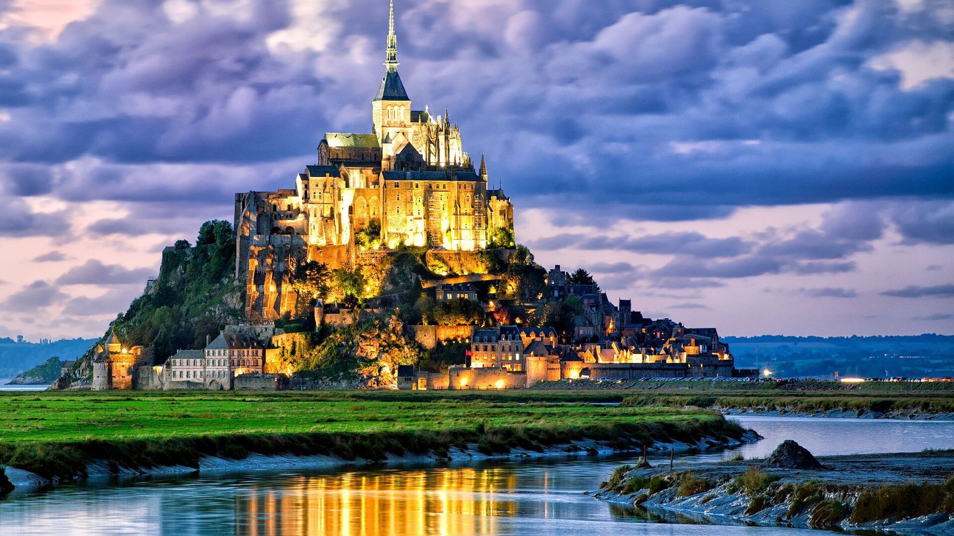 A historic castle with multiple towers and a prominent spire, situated on a hill overlooking a river.