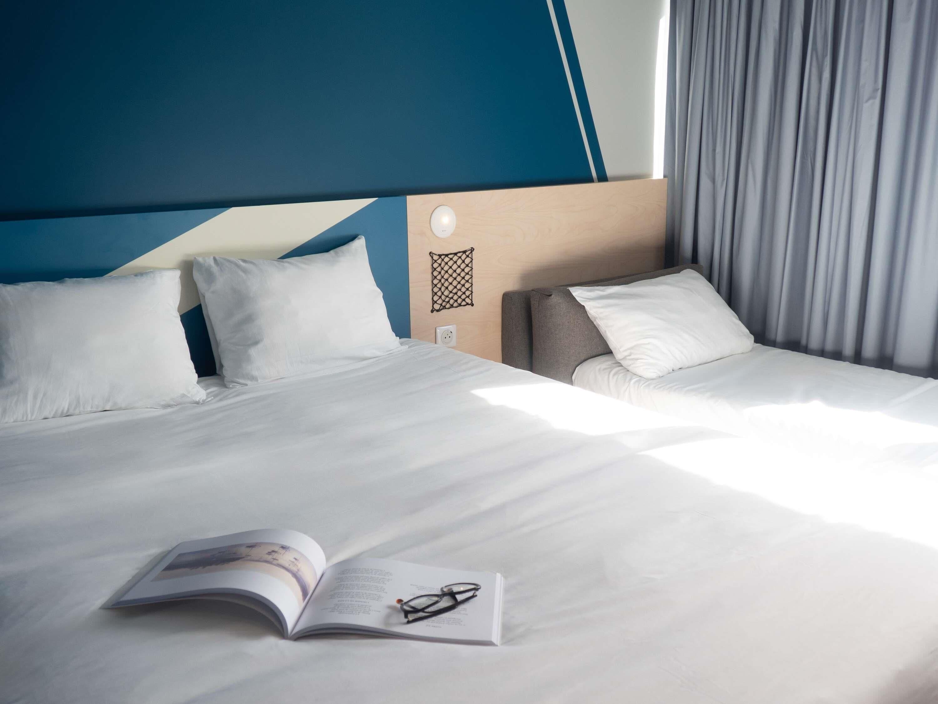 Una camera d'albergo con un letto, un comodino, una lampada da lettura e una finestra con tende.