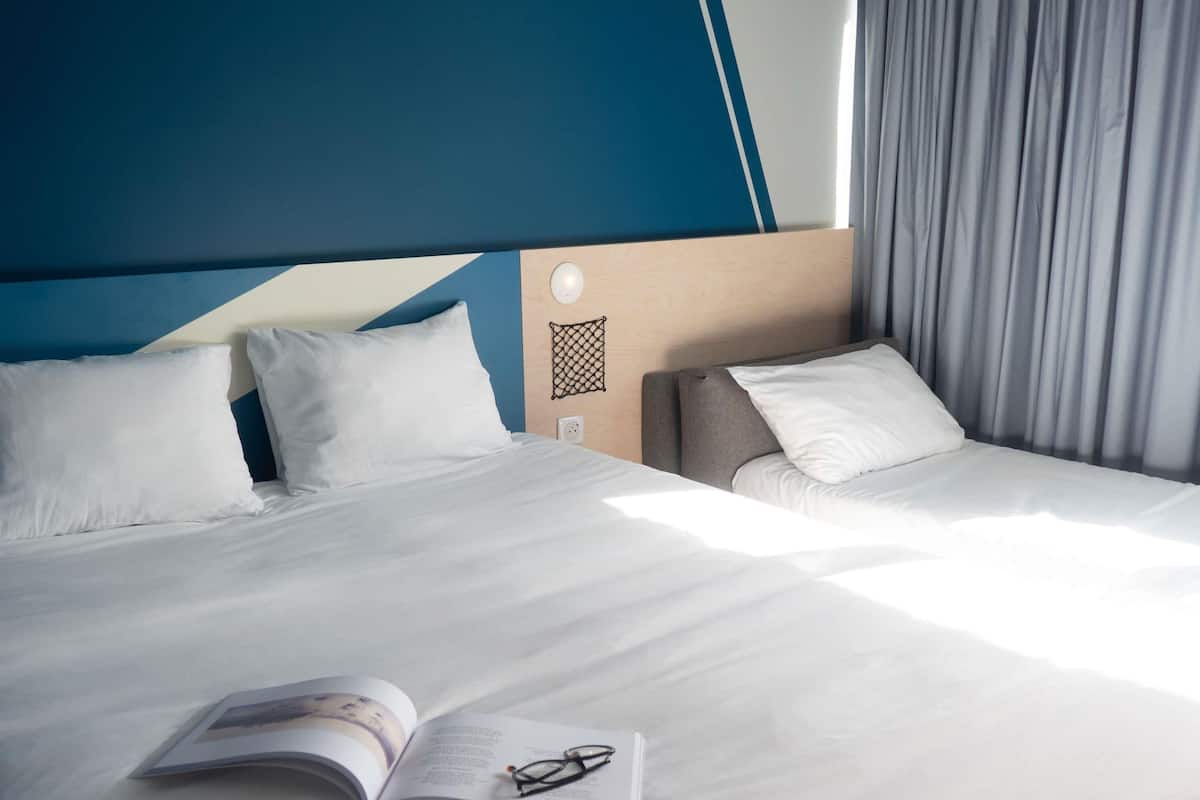 A hotel room with a bed, a bedside table, a reading lamp, and a window with curtains.
