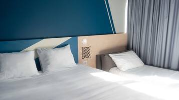 Une chambre d’hôtel avec un lit, une table de chevet, une lampe de lecture et une fenêtre avec des rideaux.