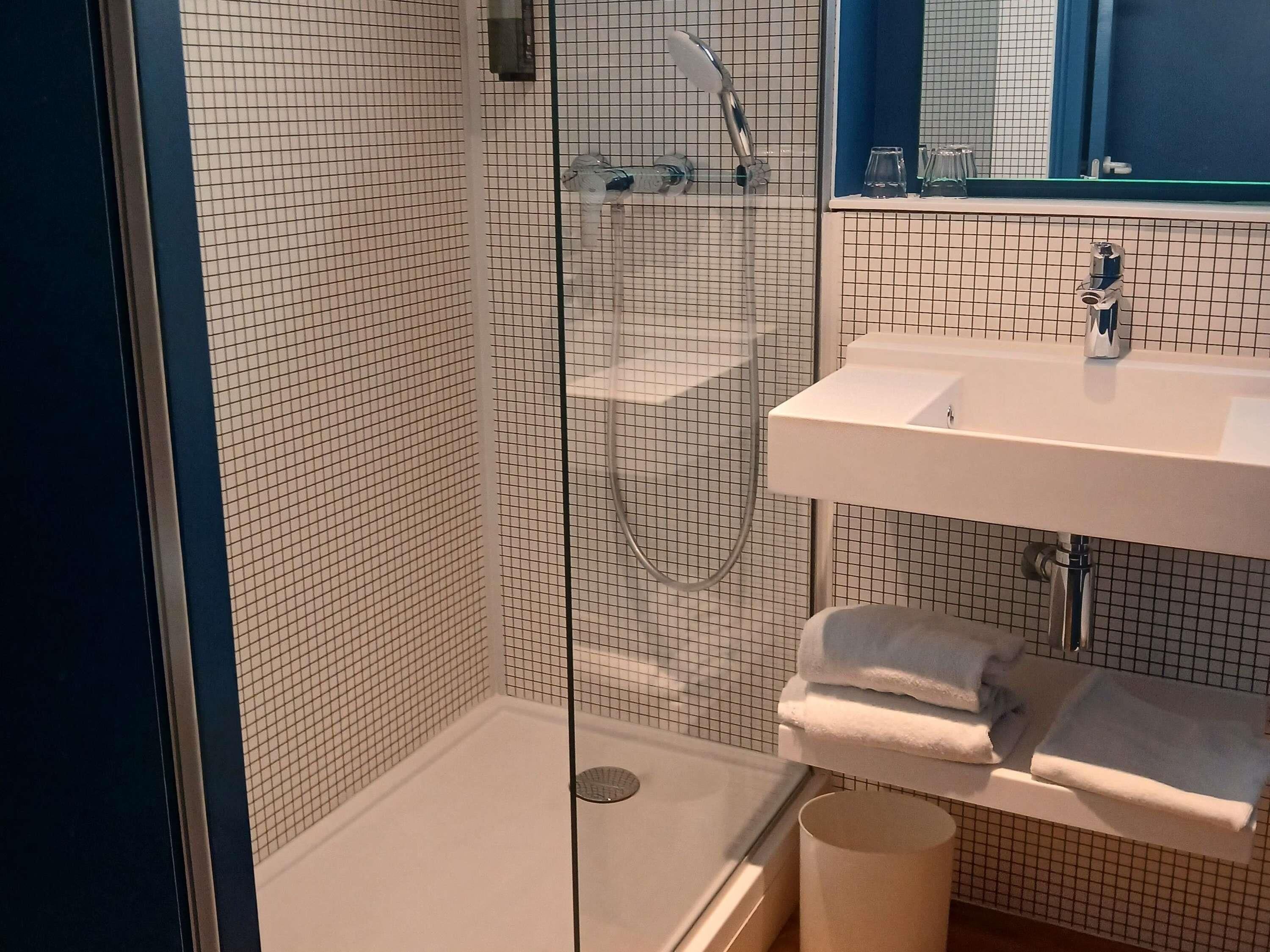 Un baño moderno con ducha envuelta en vidrio, un lavabo blanco y un espejo sobre él.