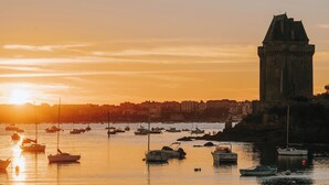 A harbor with boats at sunset, a prominent tower, and a cityscape in the background.