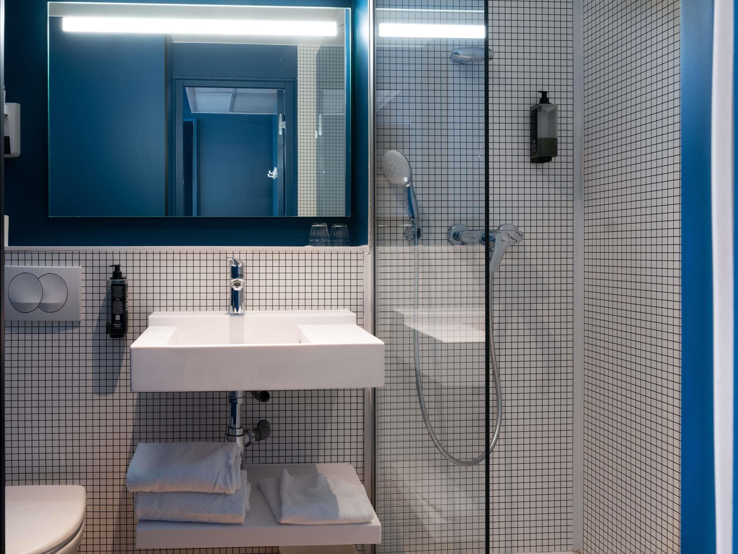 Une salle de bain avec un lavabo blanc, un miroir, un porte-serviettes et un espace douche.