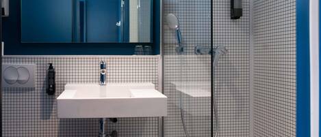 Un baño con lavamanos blanco, un espejo, toallero y zona de ducha.
