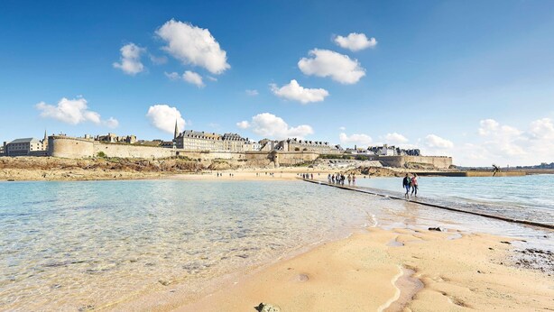 A coastal town with a prominent castle, clear blue skies, and a sandy beach.