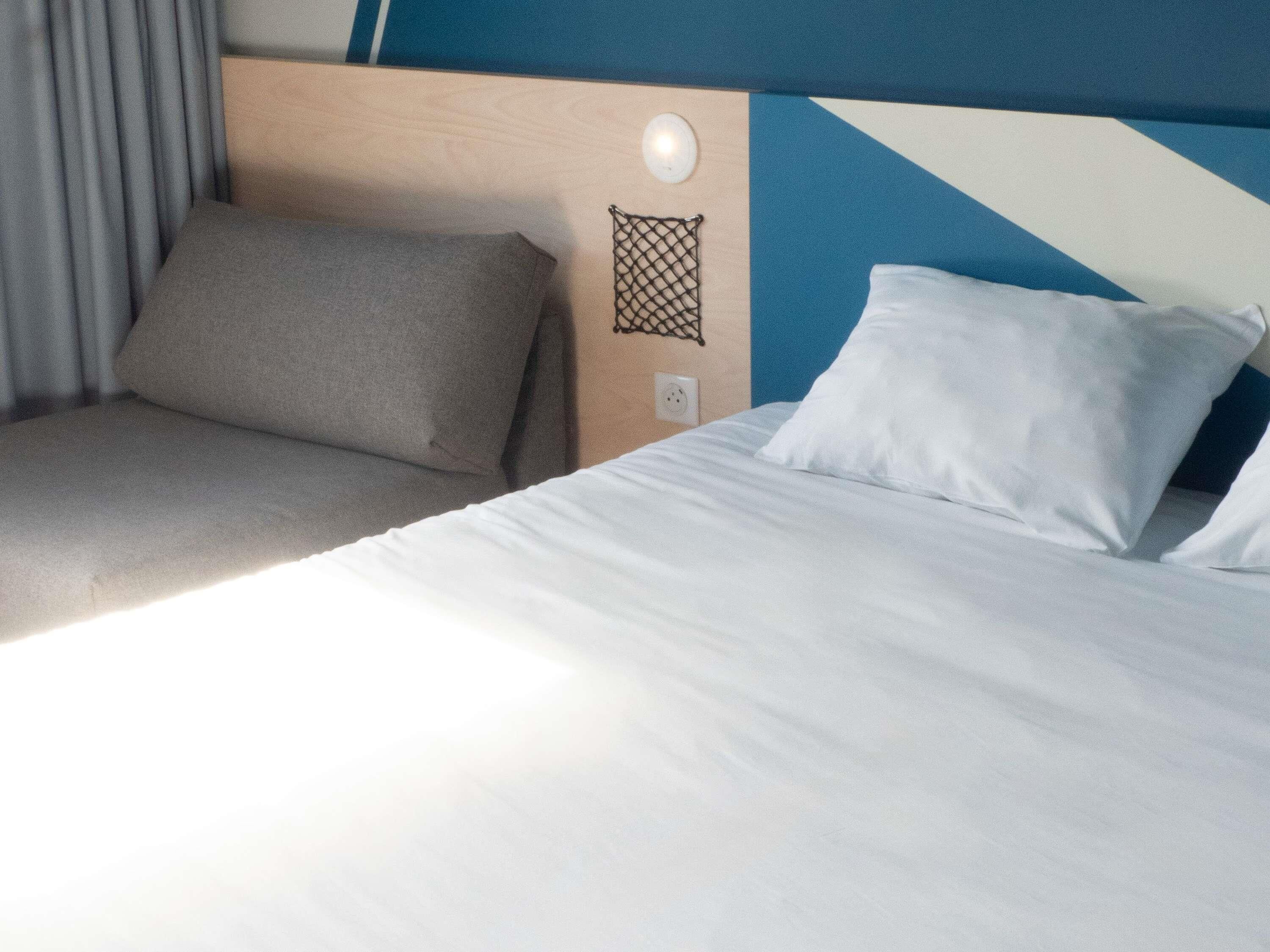 Une chambre d’hôtel équipée d’un lit, d’une tête de lit, d’une lampe fixée au mur et d’une prise de courant.