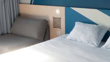 Quarto de hotel com cama, cabeceira, luminária fixada na parede e tomada.