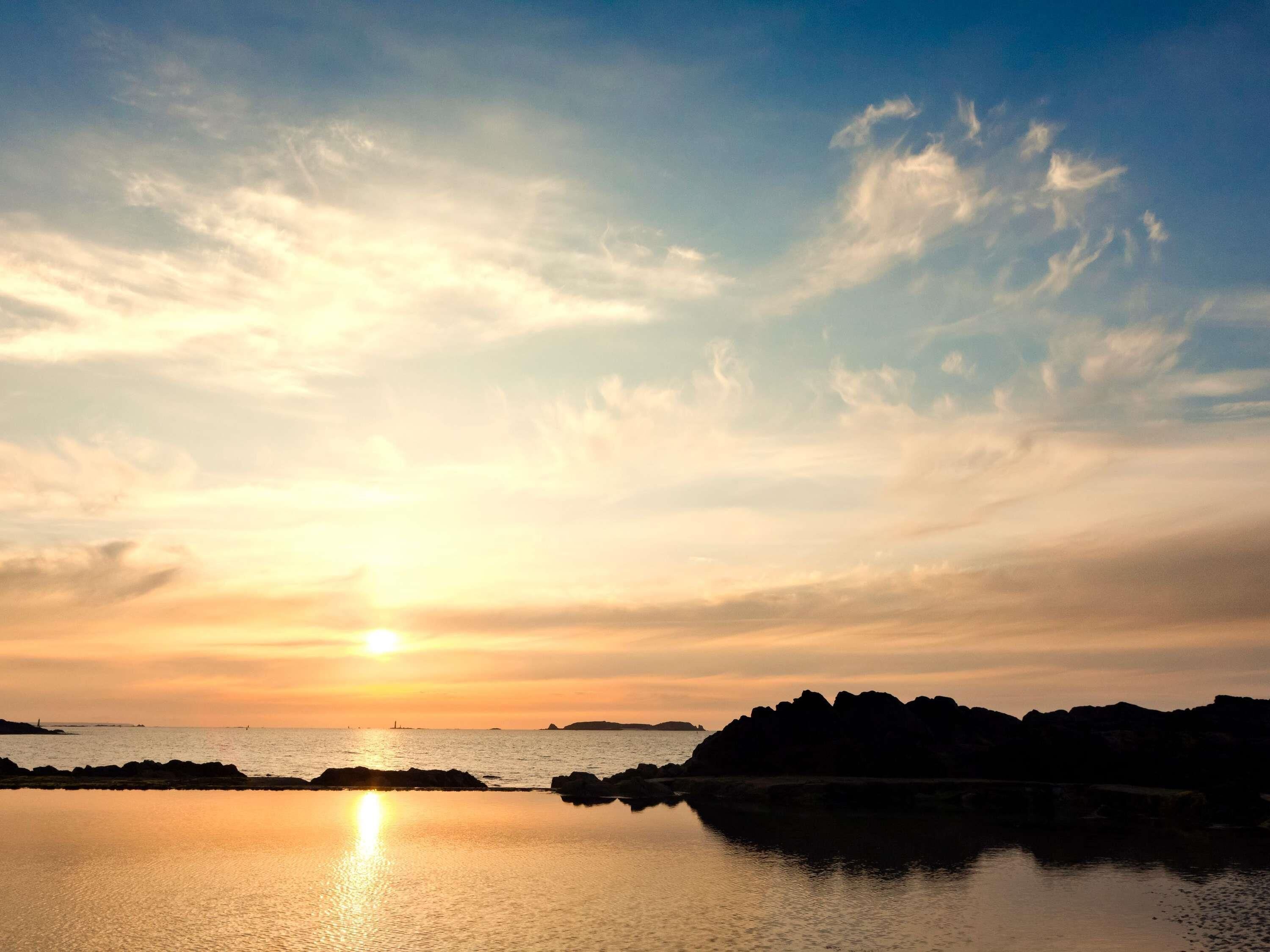 A sunset over a calm body of water with rocky formations in the distance.
