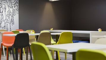 Un espace repas moderne avec des chaises et des tables aux couleurs vives, une fresque murale en noir et blanc, et un luminaire éclatant au-dessus des tables.