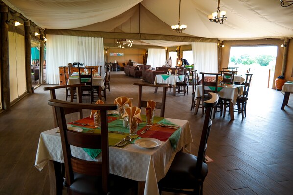Amplia zona de comedor cubierta con carpas, con varias mesas dispuestas para los huéspedes, que ofrece diferentes opciones de asientos y un candelabro central.