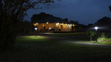 A tent-like structure with multiple light sources, surrounded by a grassy area and trees.