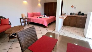A hotel room with a bed, a dining table, a kitchen area, and a living area with a sofa and chairs.